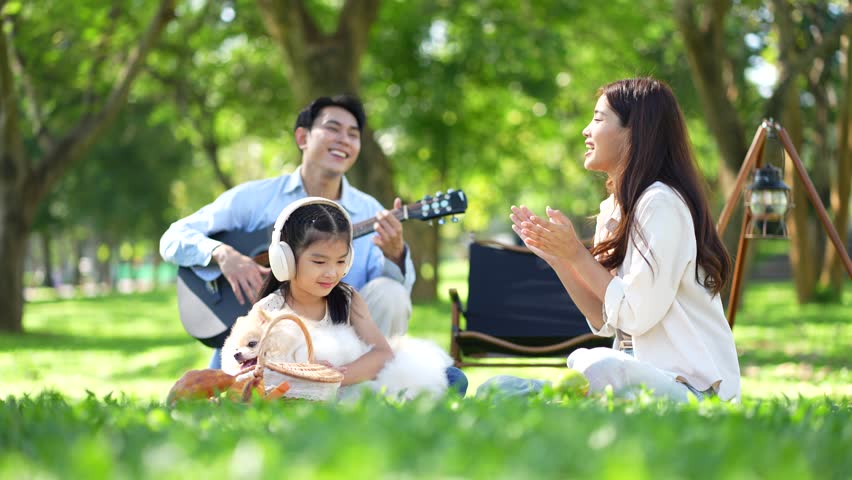 Asian family enjoying a picnic in the park on a sunny weekend. Smiling parents and kids bonding, relaxing, and spending joyful time together in nature.