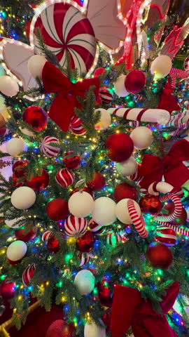 CLOSE UP, VERTICAL Vibrant Christmas tree bursts with festive spirit, adorned with red and white ornaments, glittery baubles and striped candy canes. Decorations shine brightly against dark green pine