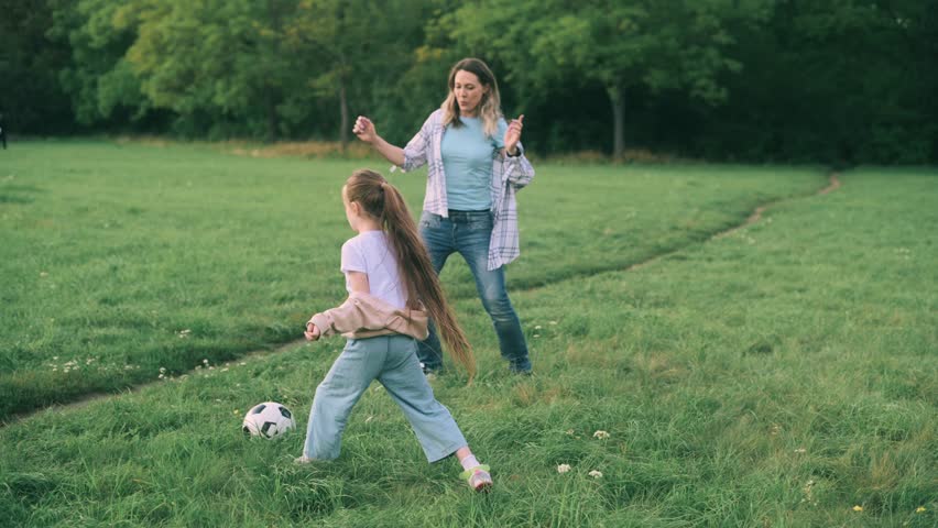 Mother and daughter are playing outdoors. An adult woman and a four-year-old girl play with a soccer ball in a park.