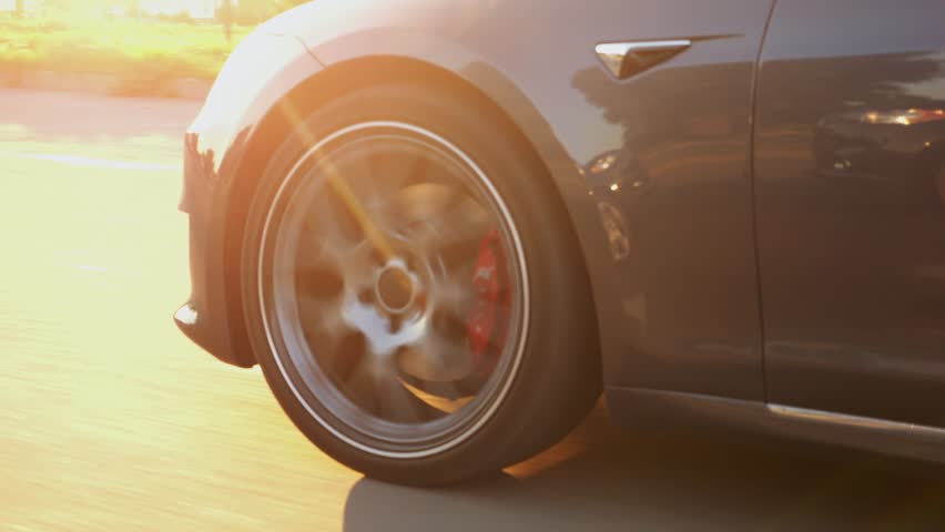 Wheel of modern electrical automobile driving at urban road on sunny day. Ecology friendly car riding moving along motorway. Electric vehicle riding through empty highway. Green innovation concept