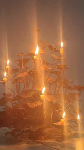 Candle flame with decorative metallic holder
A single lit candle casting a warm, steady flame that illuminates a decorative metallic holder with leaf‑like motifs and curving stems, producing soft high