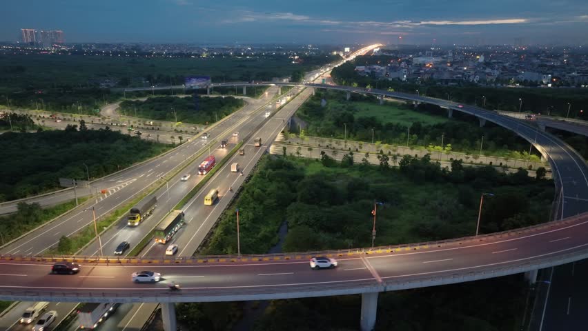 An elevated view of a large highway interchange at dusk in Hanoi, Vietnam, with cars and trucks traveling on the various lanes.