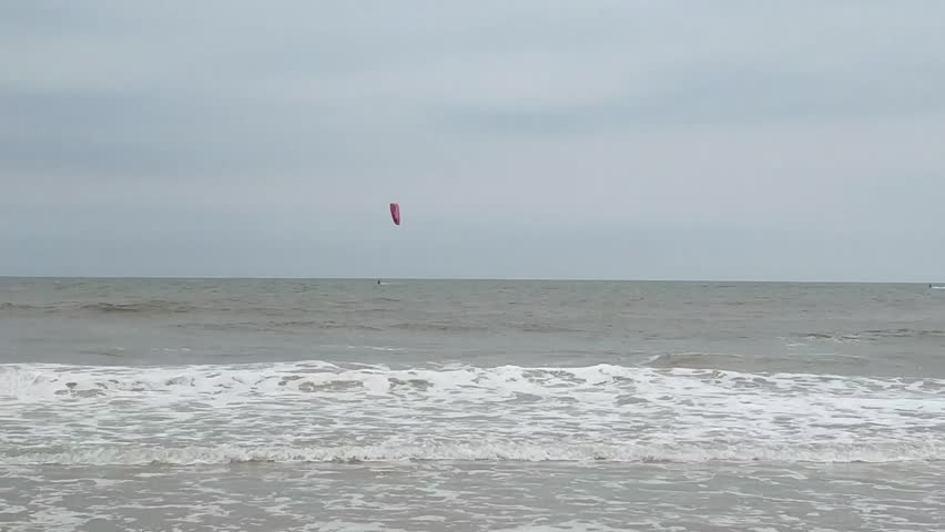 Kite surfers with colorful kites over calm sea under cloudy sky
Two kite surfers ride the gentle waves with a pink and a green kite high above the water; calm ocean and clear horizon under an overcast