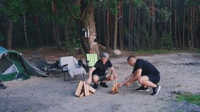 Two men light a fire in the evening forest during a hiking trip. Caucasian men relax at a campsite and prepare to cook as the sun sets over the forest. Active recreation in the wilderness. - Powered by Shutterstock - Get 15% off with code: PIKWIZARD15