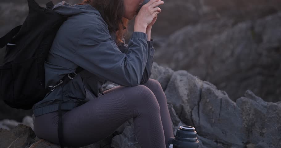 Slow motion close-up of woman hiker drinking tea and smiling.