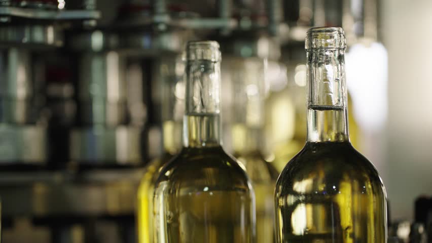 Slow motion close up of white wine bottles moving along an industrial bottling line