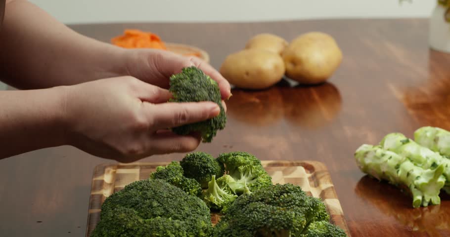 Cook Breaking fresh broccoli into florets on a wooden cutting board.