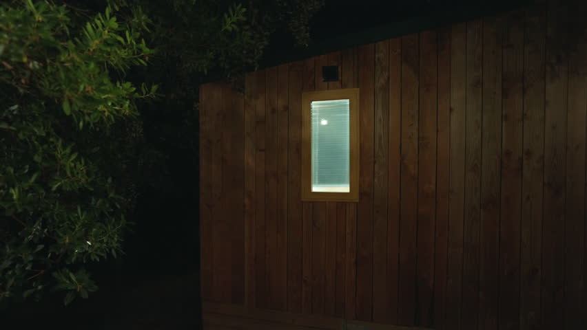 Dark exterior of wooden cabin with rectangular window lit from inside