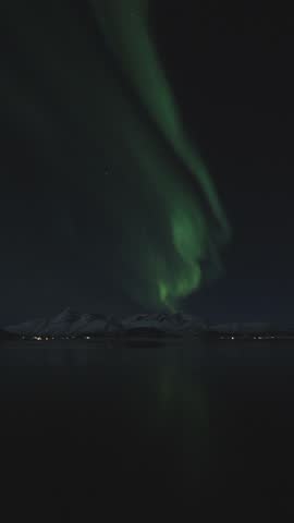 Timelapse view of green aurora with full-moon dancing over Malangen Fjord and the village of Sand in Troms, Northern Norway