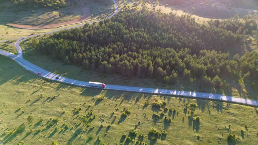 Aerial perspective of cars and a semi-truck driving on a scenic highway through a green forest