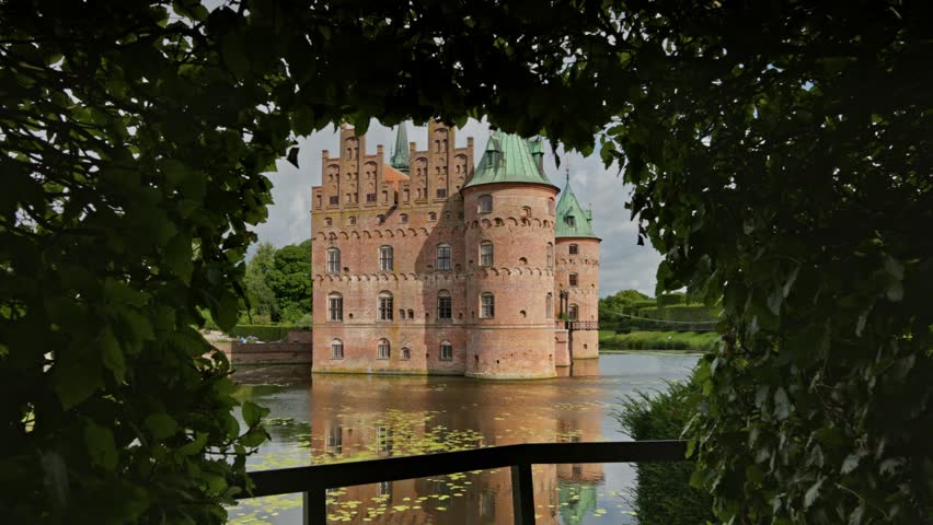 Gimbal shot of Egeskov Castle, Denmark. Egeskov Slot in Denmark - stunning Renaissance castle surrounded by lush gardens and serene waters on beautiful sunny day