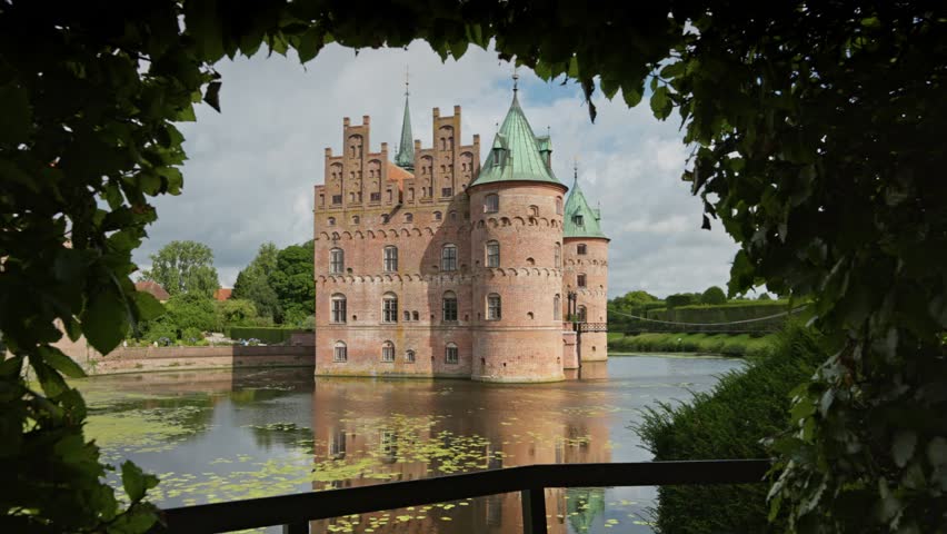 Gimbal shot of Egeskov Castle, Denmark. Egeskov Slot in Denmark - stunning Renaissance castle surrounded by lush gardens and serene waters on beautiful sunny day