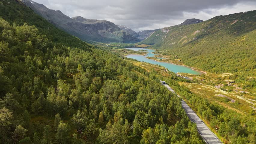 Stunning landscapes of Jotunheimen National Park with turquoise lakes and lush green hills, Norway. Traveling by camper. Car moves along road in Jotunheim National Park, aerial view