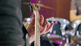 Close-up of guitarist's hand on electric guitar neck with blurred drummer in background. Dynamic atmosphere of music studio. Slow motion - Powered by Shutterstock - Get 15% off with code: PIKWIZARD15