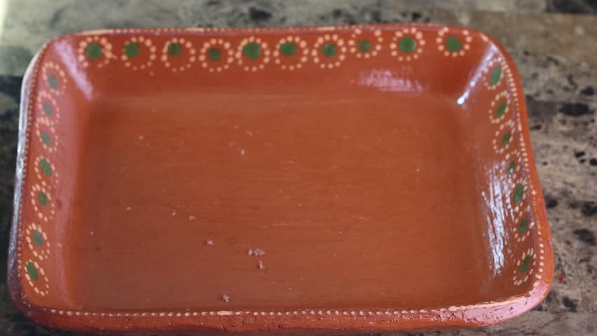 Close-up of a person placing conchas and bolillo bread onto a traditional clay tray with tongs