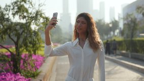 Portrait of attractive Asian woman takes selfie with smartphone in blooming city park. Happy female blogger creates content for social media followers in sunny urban garden - Powered by Shutterstock - Get 15% off with code: PIKWIZARD15