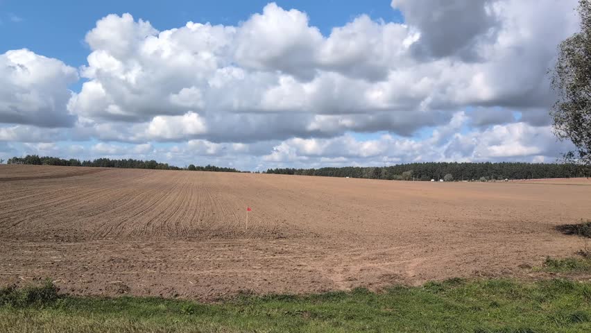 A large red tractor planting seeds in a vast, freshly tilled field under a dramatic cloudy sky, signifying farm work