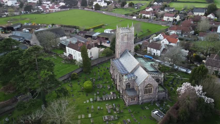 Aerial view of historic church and countryside village in England. Drone footage showing an old stone church with a cemetery and surrounding traditional buildings in rural England. 