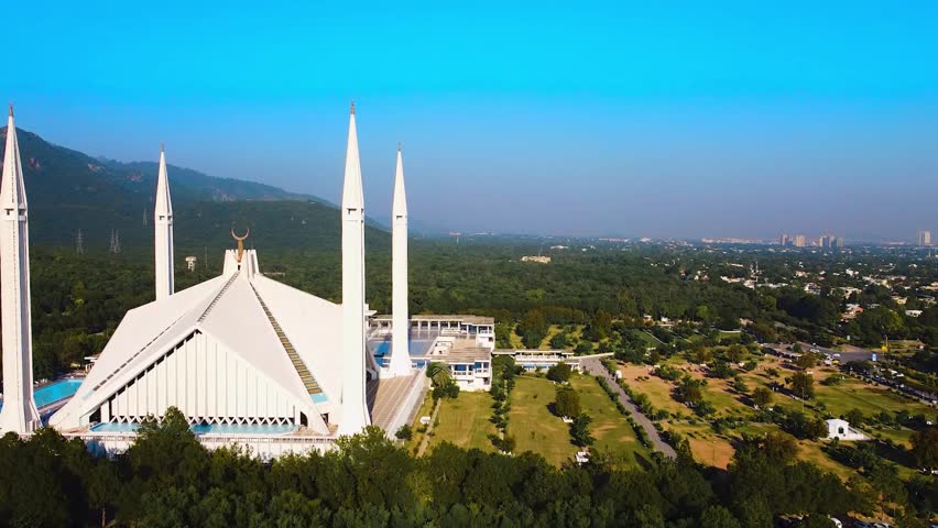 Iconic aerial drone view of the massive Faisal Mosque in Islamabad, Pakistan, set against the lush Margalla Hills and dense urban green space