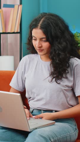 Surprised Indian young woman using laptop computer, receive mail good news message shocked by sudden victory celebrate lottery jackpot win purchases online shopping play game at home apartment on sofa