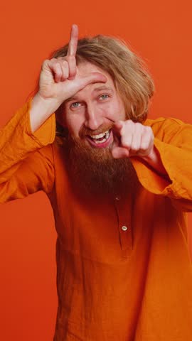 Caucasian man showing loser gesture and pointing on you, blaming accusing for unsuccess, expressing disrespect, mocking your failure, bullying abuse. Young guy isolated on orange background indoors