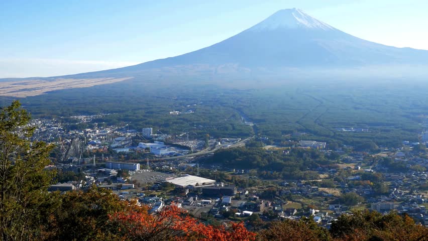 Stunning view of Mount Fuji towering over lush valleys and towns during early morning light. Vibrant foliage colors enhance scenic backdrop, showcasing Japan