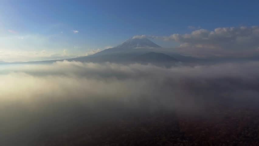 Breathtaking view of Mount Fuji emerging from thick morning mist. Soft sunlight casts a serene glow over tranquil waters. Nature