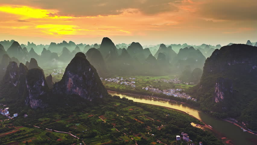 Aerial shot of the majestic karst mountain landscape with a winding river and village at sunset in Guilin, China.