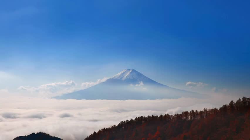 Breathtaking view of Mount Fuji standing tall above a sea of clouds. Slopes adorned with vibrant foliage showcase Japan