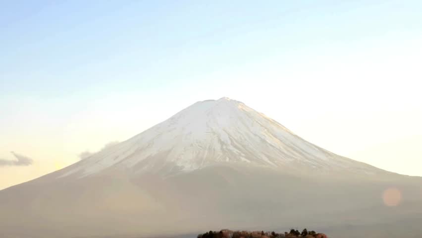 Stunning view of Mount Fuji illuminated by warm sunset light. Snow-covered summit stands elegantly against vibrant sky. Landscape highlights natural beauty of Japan.