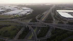 Overhead perspective of a complex highway interchange with traffic, flanked by industrial buildings and lush greenery under a hazy morning sky. - Powered by Shutterstock - Get 15% off with code: PIKWIZARD15