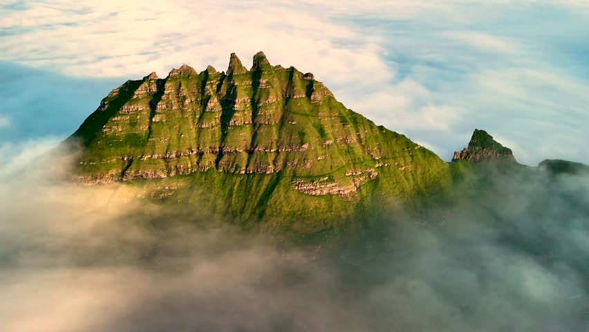 Explore the stunning Drangarnir rock formations, towering above the clouds in the Faroe Islands. This breathtaking landscape showcases nature dramatic beauty and rich greenery.