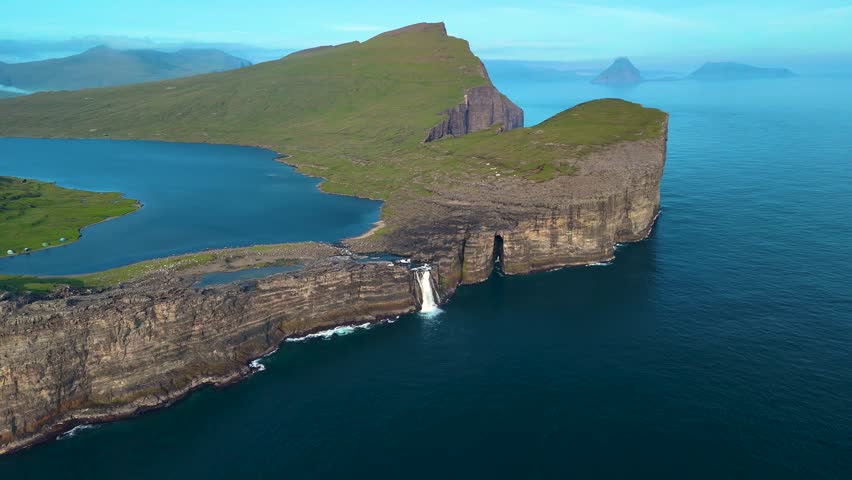 Discover the striking beauty of Lake Sorvagsvatn in the Faroe Islands, showcasing dramatic cliffs and a cascading waterfall. The serene waters reflect the vibrant landscape under a clear sky.