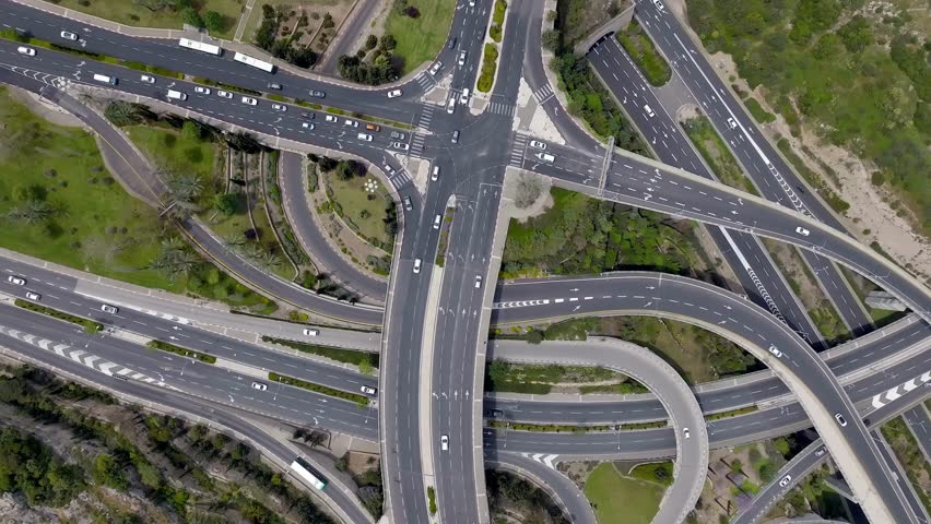 Aerial perspective captures bustling traffic at major highway interchange featuring multiple routes and vehicles traversing diverse lanes amidst lush greenery.