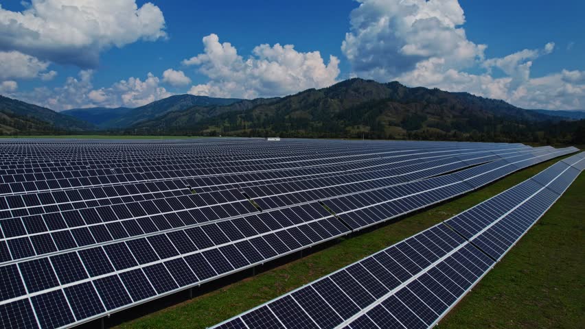 Aerial view of solar panels on sunny day in steppe mountainous area with forest, power farm producing clean energy.
