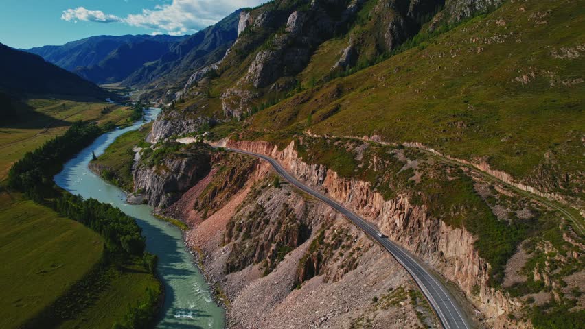 Aerial view Travel car is driving along winding mountain road in Altai beautiful nature reserve, valley of Chuya river and pine trees under clear blue sky on sunset..