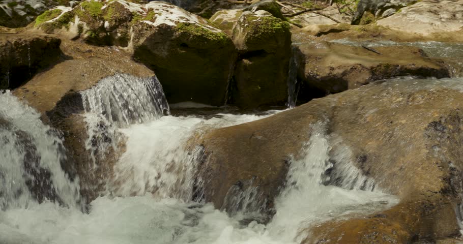Water rapids slow motion on rocky sunny stream.	
