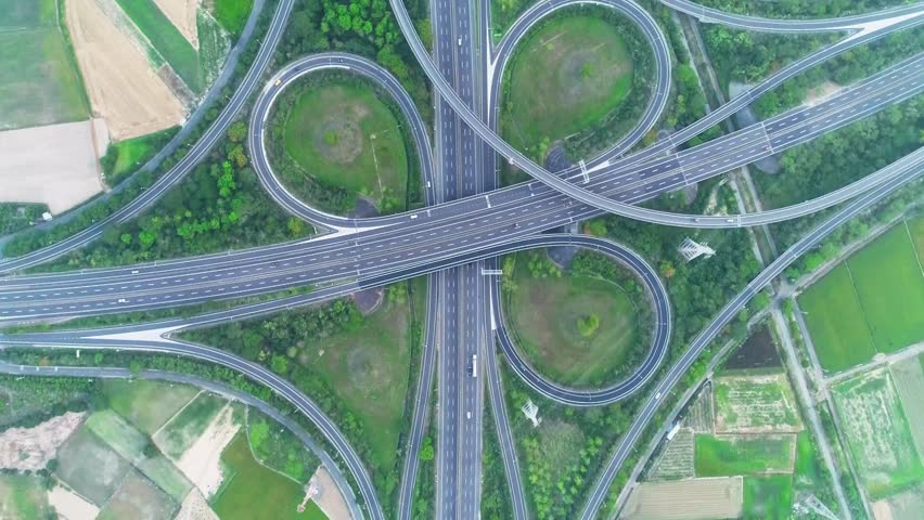Bird's eye perspective showcases intricate highway interchange weaving through lush vegetation and agricultural lands, highlighting modern infrastructure.