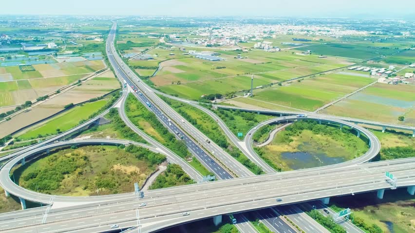 Highway interchange forms intricate patterns with vehicles traveling through greenery and farmland. A vibrant landscape showcases the contrast between urban infrastructure and nature.