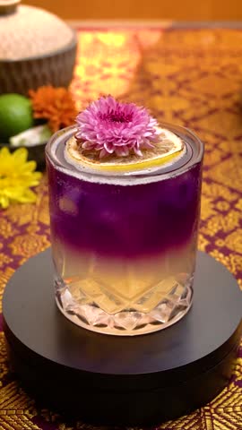 A captivating close-up shot of a refreshing Butterfly Pea Flower Tea (also known as Blue Tea) served in a short glass, slowly rotating on its axis. The beverage displays a beautiful gradient, shifting