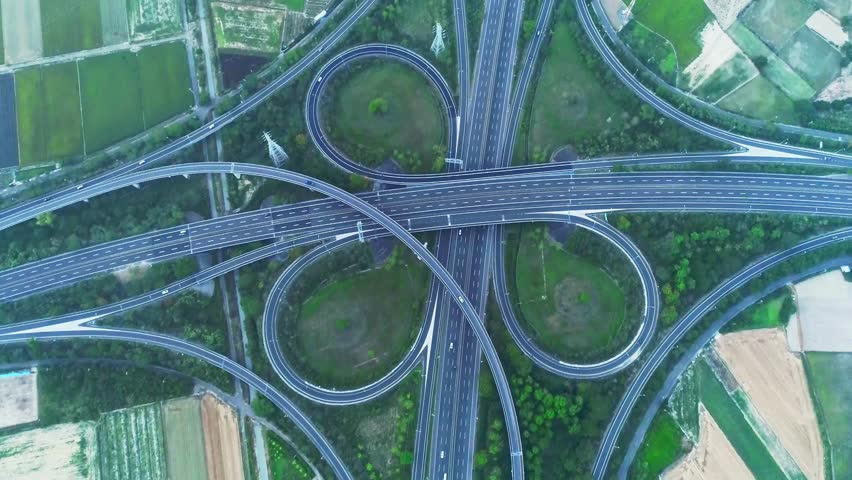 Scenic aerial perspective showcasing a complex highway interchange weaving through vibrant fields and lush greenery, illustrating transportation and nature harmony.
