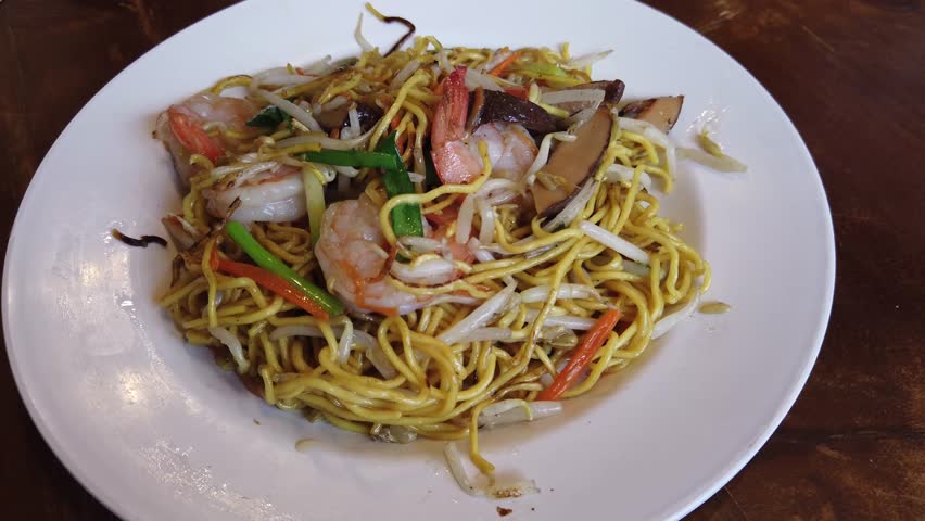 Delicious stir-fried egg noodles with shrimp, bean sprouts, and vegetables served on a white plate. Tasty Asian-style noodle dish popular in Thai and Chinese cuisine.