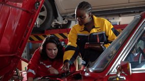 Two professional female mechanics Caucasian woman in red and a african american woman in yellow collaborate on an engine inspection of a red car using a digital tablet for diagnostics or documentation - Powered by Shutterstock - Get 15% off with code: PIKWIZARD15