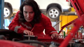 focused Caucasian female mechanic in a red uniform intently inspects the engine bay of a red car with the hood open at car repair garage. - Powered by Shutterstock - Get 15% off with code: PIKWIZARD15