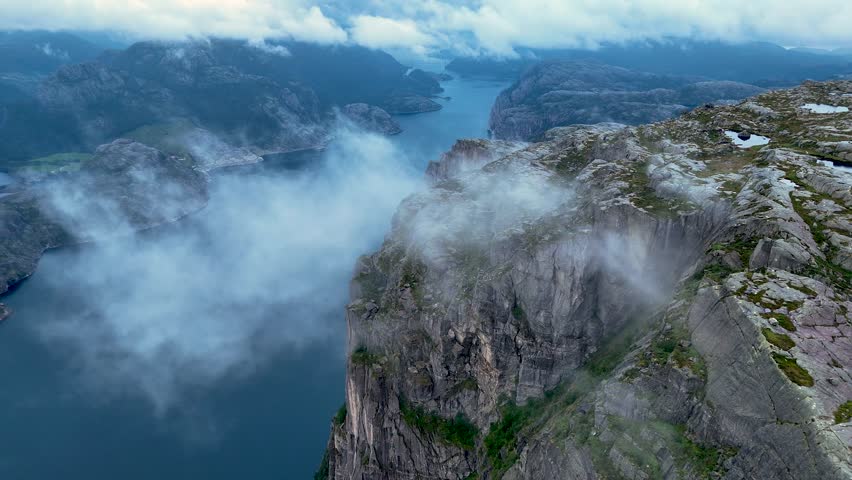 Breathtaking panoramic vistas from Preikestolen, also known as Pulpit Rock, reveal steep cliffs and a tranquil fjord below. Natures beauty unfolds as clouds drift over the landscape.