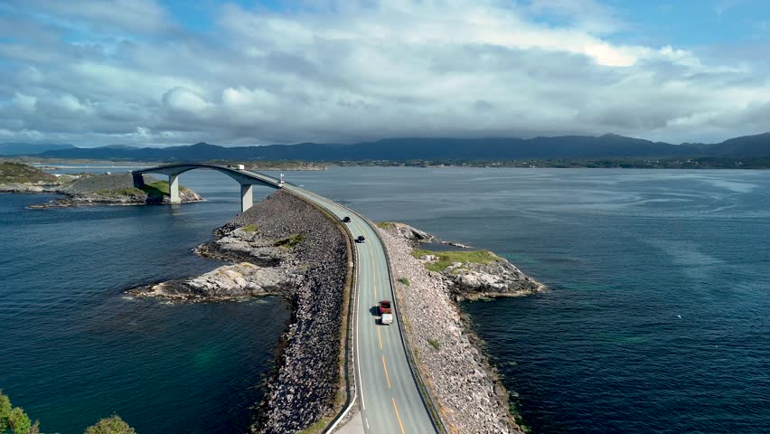Experience the breathtaking Atlantic Ocean Road in Norway, where dramatic coastal views meet engineering marvel. Cars traverse the scenic route, framed by rocky landscapes and tranquil waters.