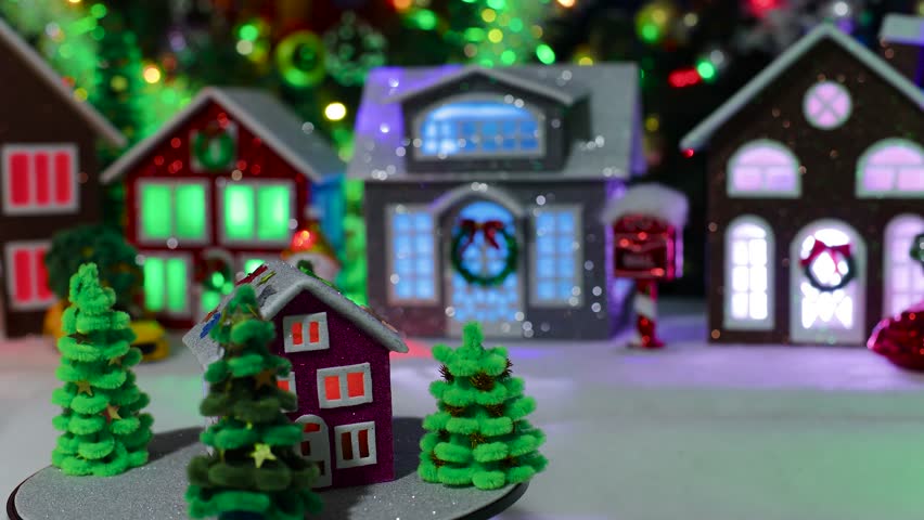 A small, dark pink house, surrounded by Christmas trees, spins in the center of a large, decorated Christmas town