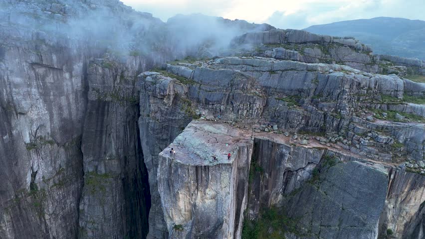 Witness the stunning landscape of Preikestolen, Norway, where towering cliffs meet the serene fjord below. Hikers marvel at this natural wonder in the golden light of dawn.