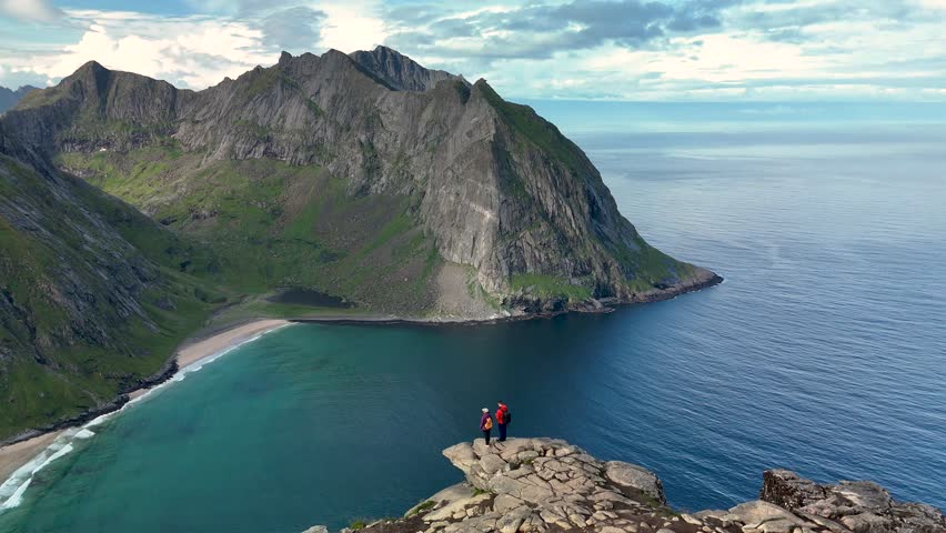 Majestic views from the Ryten Kvalvika Beach Trail in Lofoten, Norway. Hikers enjoy breathtaking landscapes with rugged cliffs and a beautiful beach below. A perfect nature escape.