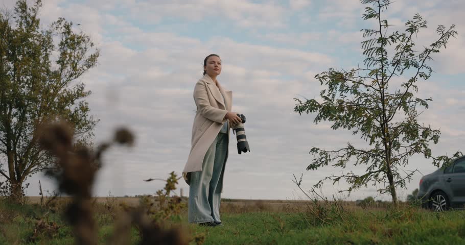 Woman photographer with big lens takes a picture at the autumn day